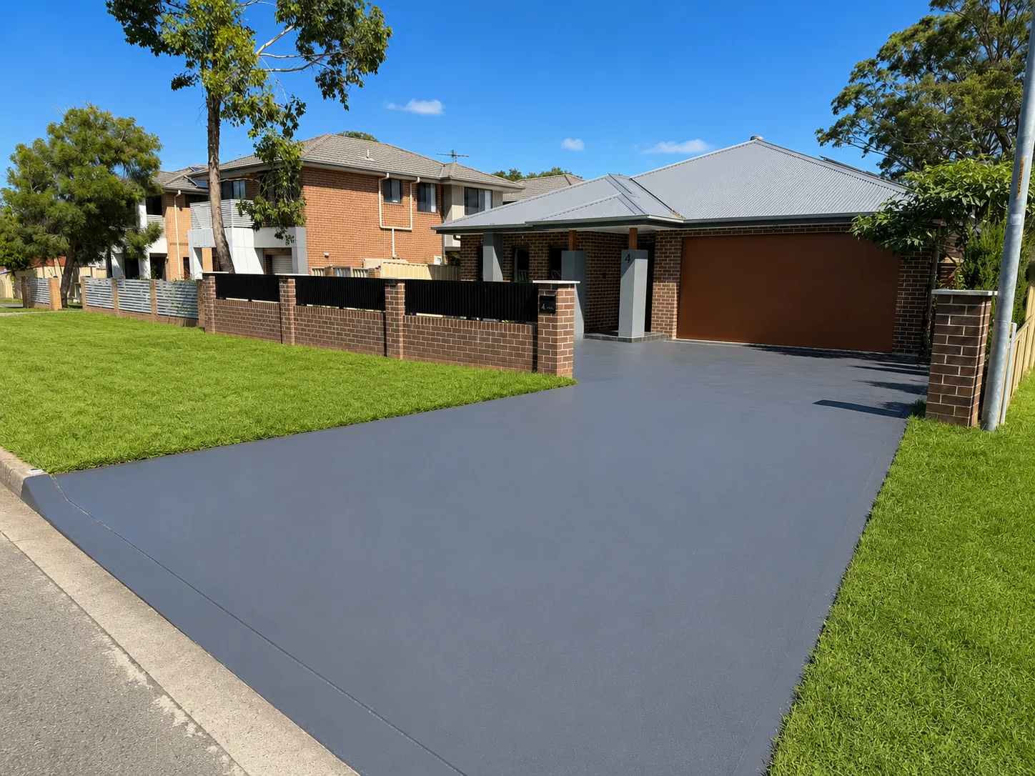 Freshly finished grey concrete driveway with new lawn and brick fence at a Sydney home by Aurum Built