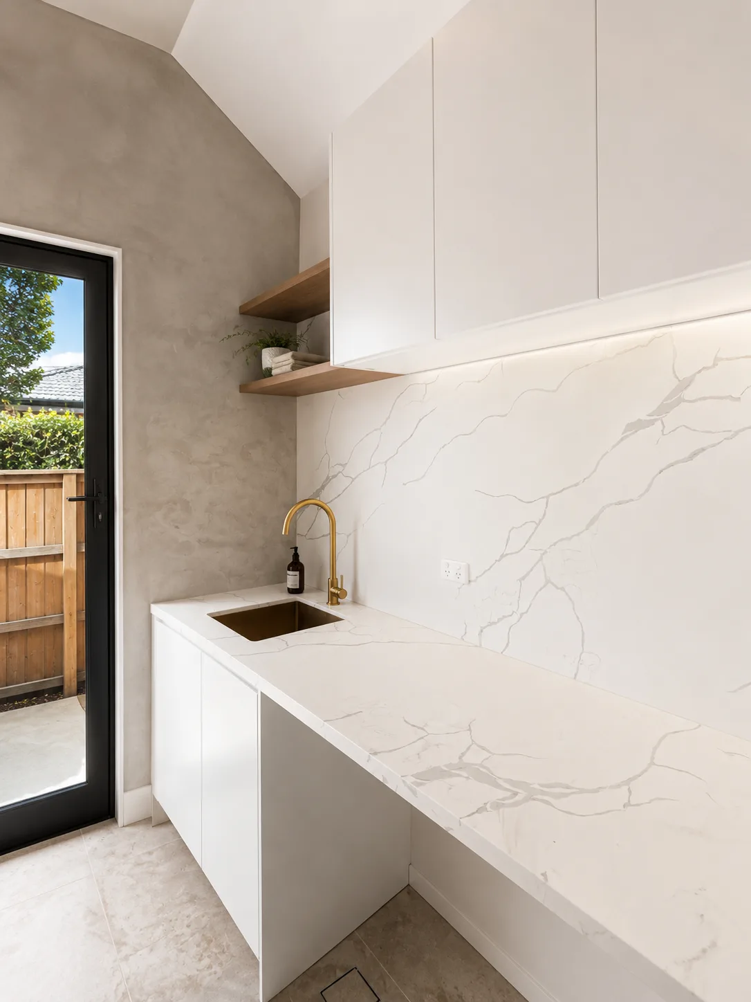 Laundry bench with marble-look surfaces, brass tapware and timber shelves